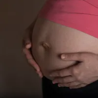 Kuvassa on raskaana olevan naisen vatsa. Vatsa on paljaana ja nainen pitää käsiään vatsan ympärillä.