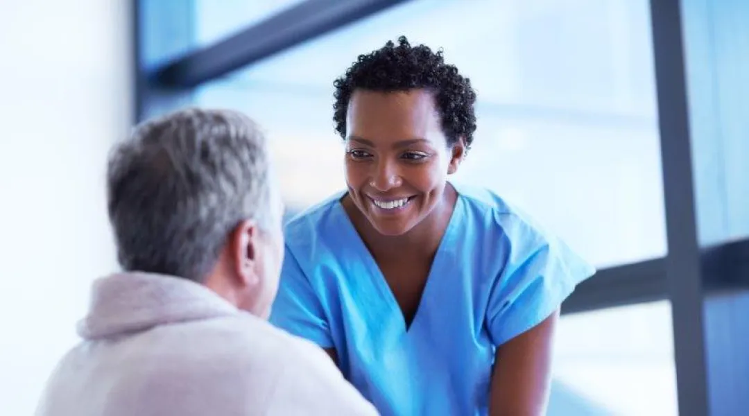 Tummaihoinen hoitaja katsoo hymyillen potilasta.