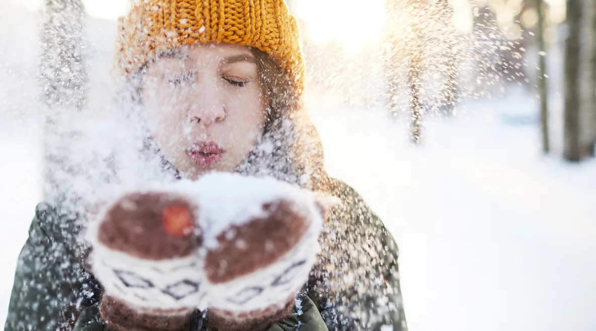 Kuvassa nainen puhaltaa käsistään lunta