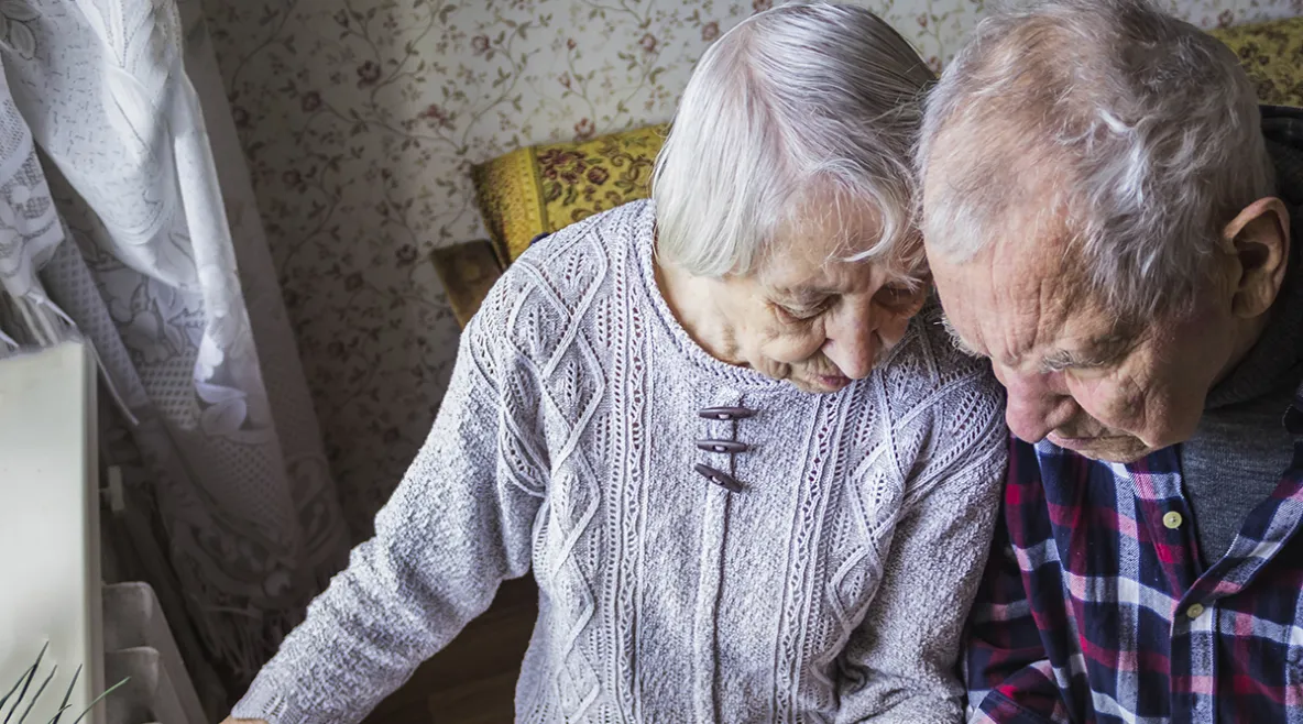 Kaksi vanhusta istuu tuolissa ja katsoo alaspäin.