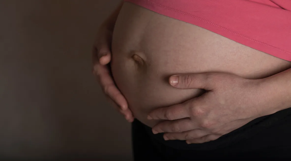 Kuvassa on raskaana olevan naisen vatsa. Vatsa on paljaana ja nainen pitää käsiään vatsan ympärillä.