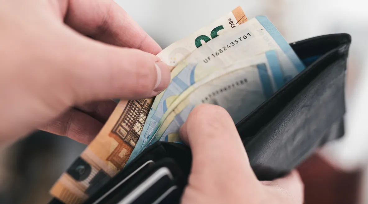 Kädet pitävät lompakkoa, josta otetaan muutama seteli tutkittavaksi