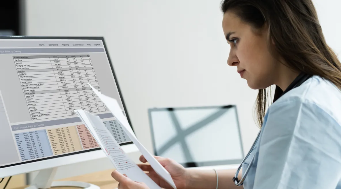 Hoitaja katsoo papereita tietokoneen ääressä. 