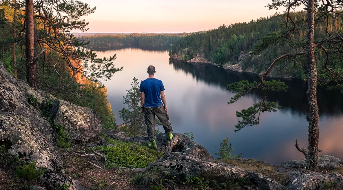 Mies seisoo kalliolla ja katsoo järvelle.