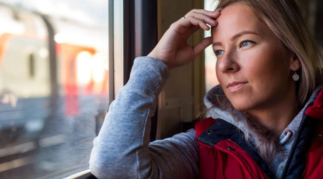vaaleahiuksinen nainen katselee junan ikkunasta