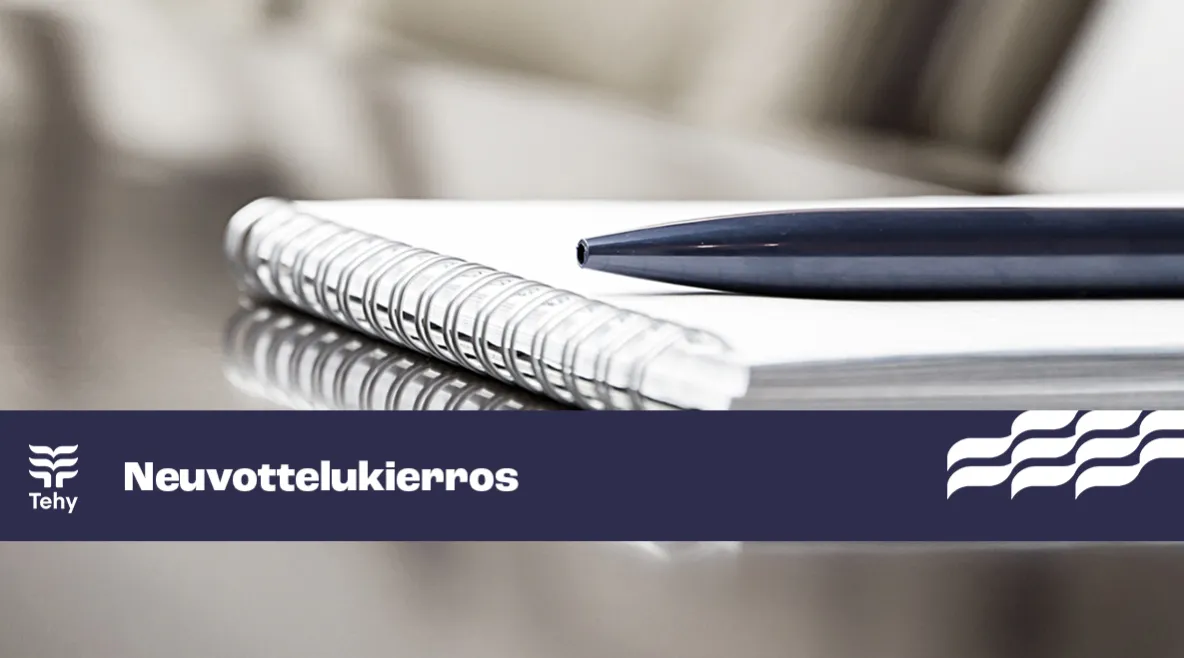 Neuvottelupöytä, jossa lehtiö ja kynä. Sininen nauha, jossa teksti &quot;neuvottelukierros&quot;.