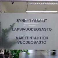 Sairaalan ovessa kyltti, jossa lukee synnytyssalit, lapsivuodeosasto, naistentautien vuodeosasto.