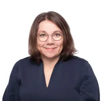 Tummahiuksinen nainen hymyilee, silmälasit päässä.