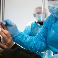 Suojavarusteisiin pukeutunut hoitaja ottaa koronanäytettä potilaan nenästä.