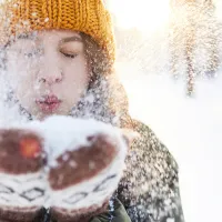 Kuvassa nainen puhaltaa käsistään lunta