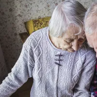 Kaksi vanhusta istuu tuolissa ja katsoo alaspäin.