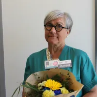 Silmälasipäinen nainen seisoo kukkakimppu kädessään.