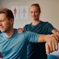 Fysioterapeutti venyttää ja tutkii potilaan käsivartta vastaanotolla.