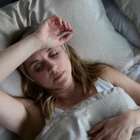 Väsynyt nainen vuoteessa käsi otsalla. 