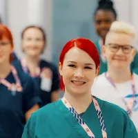 Kuvassa hoitajia, jotka hymyilevät. Hoitajilla on kaulassa Tehyn kaulanauha.