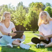 Kaks opiskelijanaista nurmikolla, aurinko paistaa