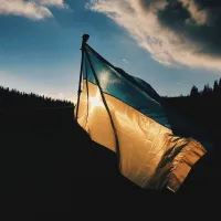 Ukrainan lippu liehuu iltahämärissä. Taustalla metsää.