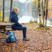 nainen istuu tuolilla retkipaikalla  metsässä syksyllä lammen rannalla