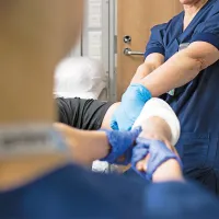Kaksi hoitajaa käsittelee potilaan kipsattua kättä. 
