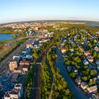 Ilmakuva Tampereen kaupungista kesäiltana, etualalla rautatie ja asuinalue värikkäine taloineen, vasemmalla suuri vesialue ja satama-alue, taustalla keskustan rakennuksia ja näkötorni, oikealla toinen vesialue ja vihreitä metsäalueita.
