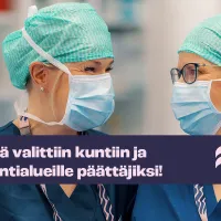 Kaksi sairaanhoitajaa maskit yllään katsoo hymyillen toisiinsa. 