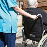 Hoitaja työntää hoivakodin asukasta pyörätuolissa ulkona.