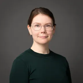 Silmälasipäinen nainen katsoo kameraan.