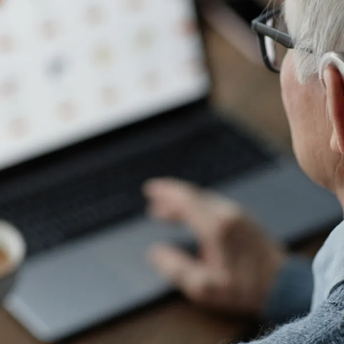 Tuoreen väitöstutkimuksen mukaan digipalvelujen onnistumista pitäisi mitata sillä, saako ihminen avun. Vanhus kuulokojeen kanssa käyttämässä tietokonetta.