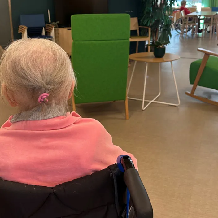Vanhus istuu pyörätuolissa selin kameraan hoivakodin aulatilassa.