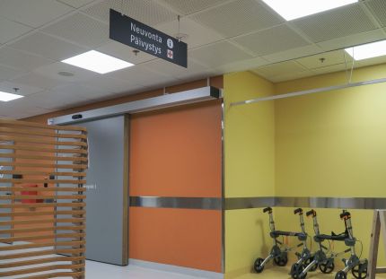 Kainuun hyvinvointialue aloittaa yt-neuvottelut. Kuvassa Kainuun keskussairaalan käytävä, jossa värikkäät seinät ja kävelytukia seinän vieressä.