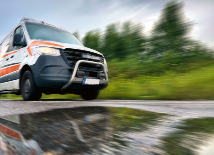 Ambulanssi ajaa kovaa vauhtia asfalttitietä, jonka päällä vesilammikko.