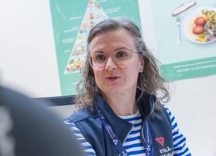 Hyvinvointivalmentaja Ulla Heimonen työhuoneessaan. Seinällä kuvia lautasmallista.