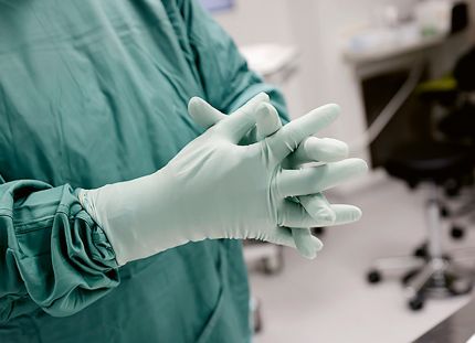 Hoitaja leikkaussalissa suojavarusteissa asettaa kätensä yhteen.