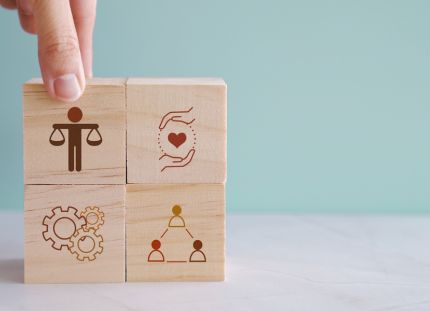 Uudistetuissa eettisissä ohjeissa käsitellään muun muassa rajallisten voimavarojen kohdentamista, teknologian roolia sekä ammattilaisten kokeman eettisen kuormituksen tunnistamista. Käsi asettelee puupaloikoita pinoon, jossa erilaisia symboleita.