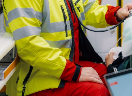 Hyvinvointialue päätti ensihoitajan työsuhteen perusteettomasti. Ensihoitaja kuuntelee potilaan hengitysääniä ambulanssissa.