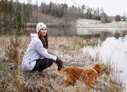 Kätilö Miia Sillman kuuraisessa talvimaisemassa vedenäärellä koiran kanssa.
