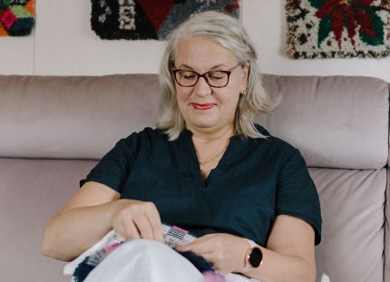 Marja-Liisa Haapakorva viimeistelee ryijyä olohuoneensa sohvalla.