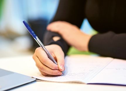 Cecilia Suomi laskemassa lääkelaskuja. Lähikuva käsistä ja laskuvihkosta.