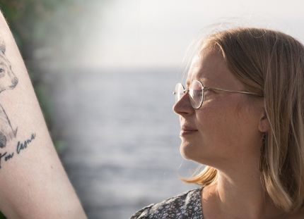 Kuva kädestä, jossa karhutatuointi. Oikealla Sairaanhoitaja Mirva Virtanen katsoo horisonttiin taustalla meri.
