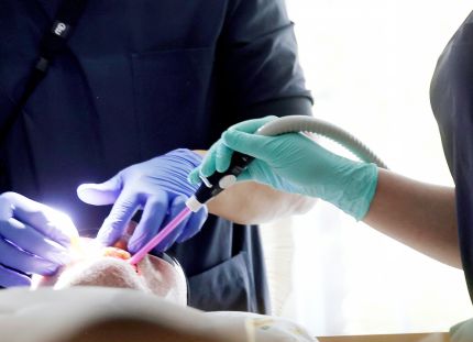 Hammashoitaja avustaa hammaslääkäriä. Potilas kuvassa suu auki.