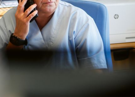 Terveydenhuollon ammattilainen työpisteellä puhelimessa, päällä vaaleansininen työasu