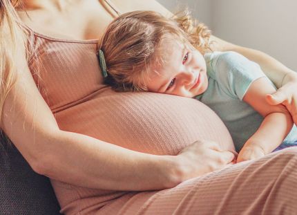 Raskaana oleva nainen, johon isompi lapsi nojaa.