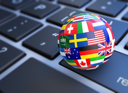 Tietokoneen näppämistön päällä pallo, jossa on eri maiden lippuja. 