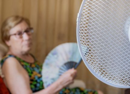 Ilmastokriisi tuottaa uudenlaisia vaikeuksia erityisesti haavoittuvassa asemassa olevien vanhusten hoitoon. Vanhus istuu tuolissa tuulettimen vieressä ja löyhyttää ilmaa viuhkalla.