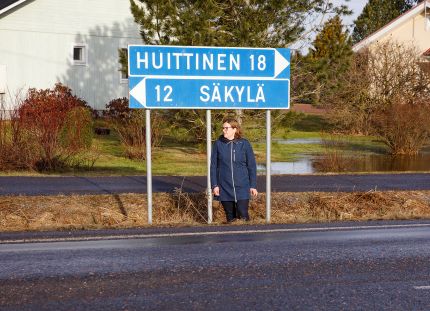 Esihenkilö Minna Kyttänen seisoo tien pientareella. Tienviitoissa lukee "Huittinen 18" ja "Säkylä 12".