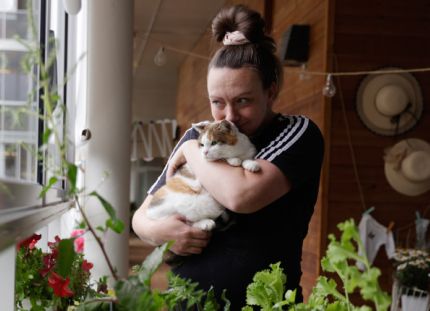 Lähihoitaja Kiia Malin Miiru-kissa sylissään Kontulan seniorikeskuksen parvekkeella.
