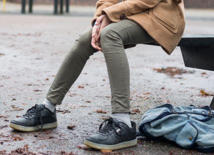 Lasten ja nuorten keskinäinen kiusaaminen rakentuu vähitellen. Yksinäinen lapsi koulun pihalla. Reppu maassa ja syksyisiä lehtiä asfaltin pinnalla.