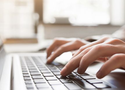 Henkilö kirjoittamassa someen tekstiä kannettavalla tietokoneella.