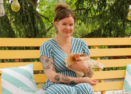 Julia Lehtilä istuu keltaisessa pihakeinussa kana sylissään.