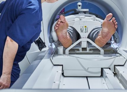 Potilas menossa magneettikuvaukseen koneeseen. Hoitaja varmistamassa vierellä.